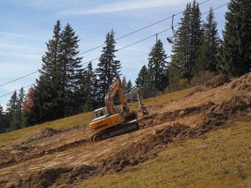 Land surveyor measuring elevation changes between steep ridges on a compact residential construction site.